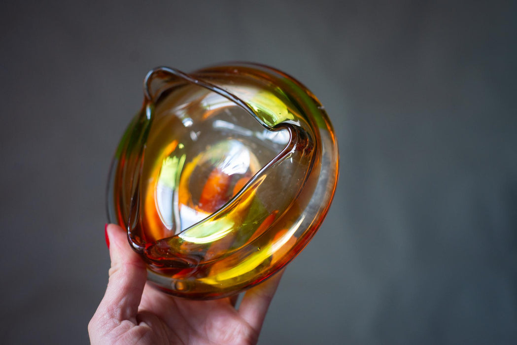 A hand holding a glass bowl with a colorful, abstract design.