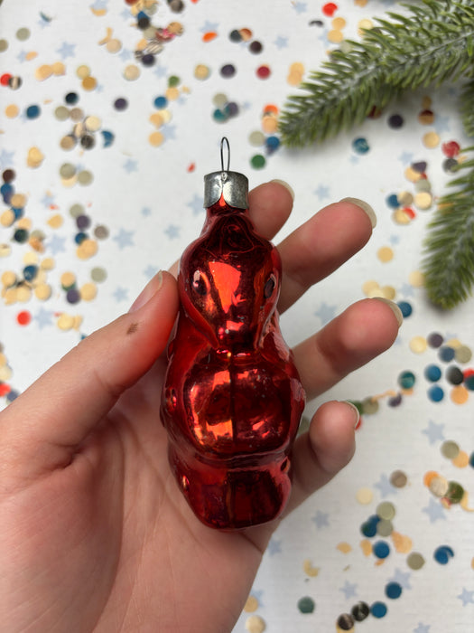 A hand holding a shiny red ornament against a background of colorful confetti.