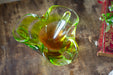 A green glass bowl with a curved shape sits on a wooden surface, with a red and gold book visible in the background.