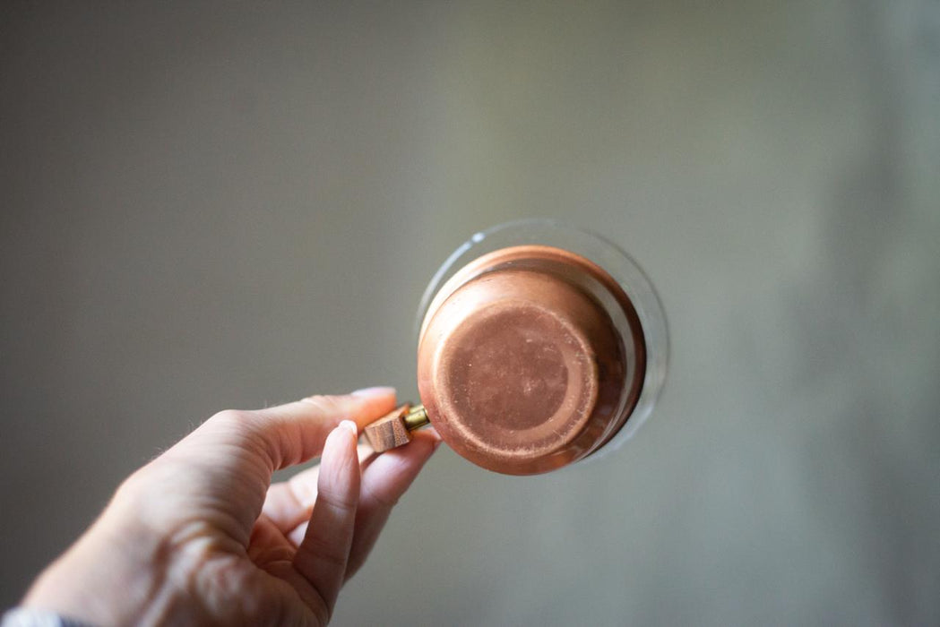 A hand holding a copper-colored metal container against a blurred background.