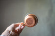 A hand holding a copper-colored metal container against a blurred background.