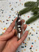 A hand holding a small, ornate glass ornament against a background of colorful confetti and a pine branch.