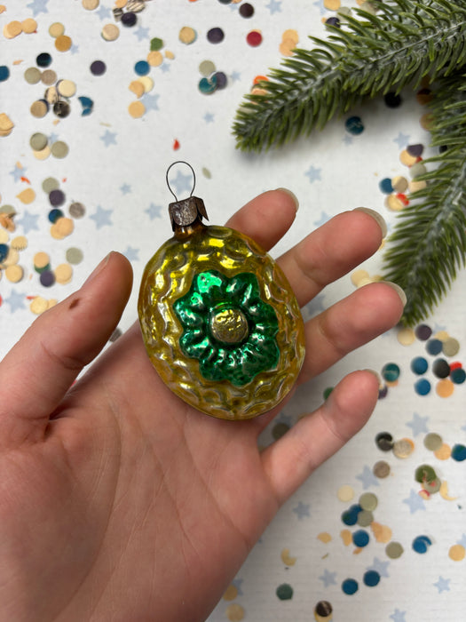 A hand holding a small, ornate ornament with a green and gold design, surrounded by colorful confetti.