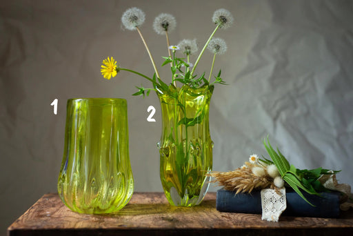 two green vases with flowers and greenery, placed on a wooden surface.