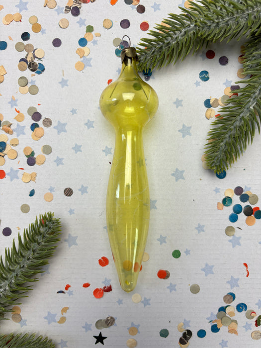 a yellow ornament with a pointed end, surrounded by confetti and green pine branches.
