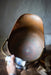 A hand is holding a blue and white ceramic object, which appears to be a small bowl or dish, and is being used to clean a copper-colored metal object, possibly a pot or pan, on a wooden surface.