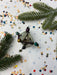 a Christmas ornament with a star-shaped design, surrounded by pine branches, confetti, and other festive decorations.