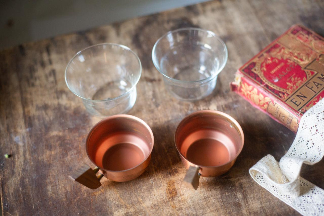 two empty copper-colored bowls and a red book with gold lettering on a wooden surface.