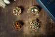 a collection of ornate brooches and jewelry pieces, including a large diamond-encrusted brooch, a smaller brooch with a floral design, and a few other pieces, all resting on a wooden surface.