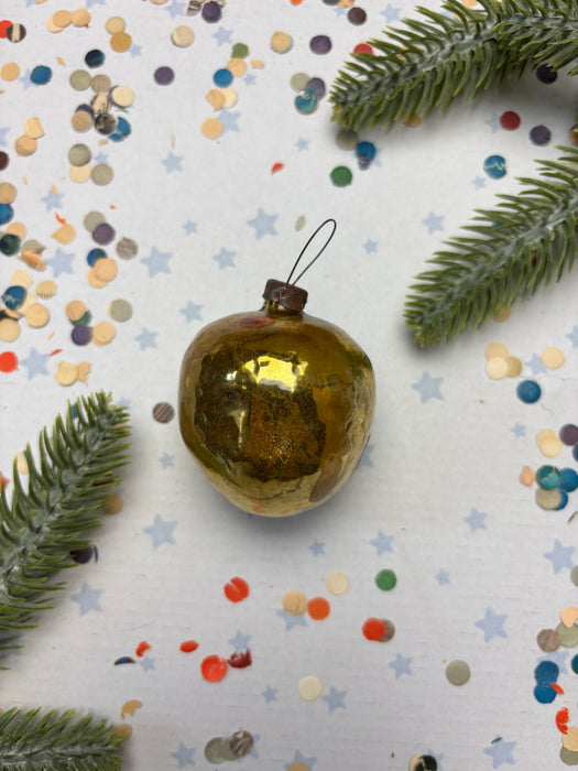 a golden ornament with a black string, surrounded by confetti and a sprig of greenery.
