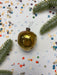 a golden ornament with a black string, surrounded by confetti and a sprig of greenery.