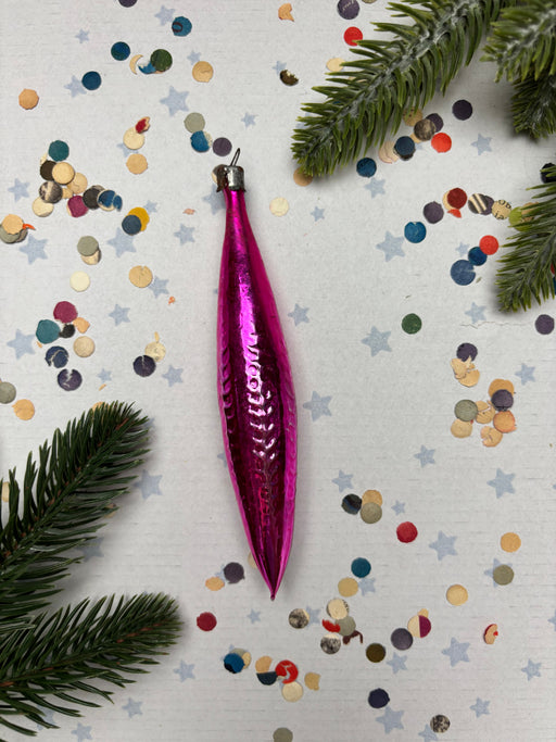 A pink ornament is surrounded by colorful confetti and pine branches on a white background.