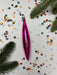 A pink ornament is surrounded by colorful confetti and pine branches on a white background.