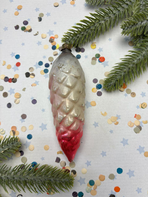 A vintage Christmas ornament with a red and white color scheme is displayed on a white background, surrounded by pine branches and confetti.