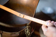 A person's hand is holding a wooden ruler with measurements on it, which is placed next to a large, ornate brass container.