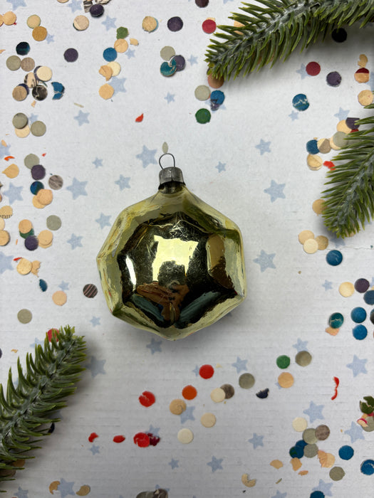 a golden ornament with a reflective surface, surrounded by colorful confetti and pine branches.