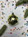 a golden ornament with a reflective surface, surrounded by colorful confetti and pine branches.