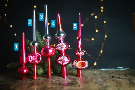 A collection of six colorful Christmas ornaments, each with unique designs, arranged on a wooden surface against a dark background with twinkling lights.
