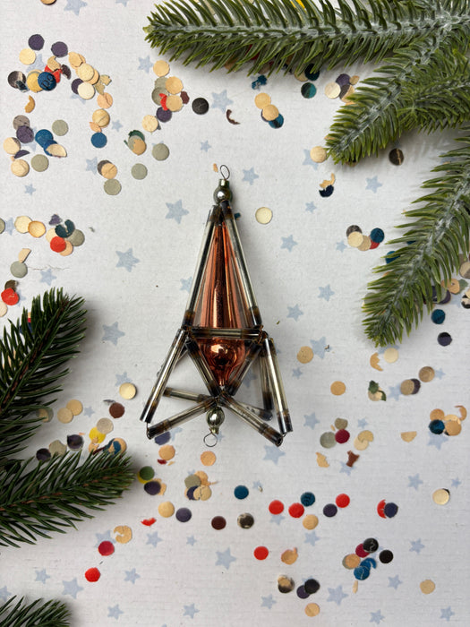 a metallic ornament with a triangular shape, surrounded by colorful confetti and pine branches.