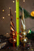 two ornate Christmas tree ornaments, one in gold and the other in copper, placed next to a green pine branch with twinkling lights.