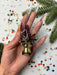 A hand holding a decorative piece with metallic and colorful elements, surrounded by confetti and pine branches.