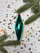 a green ornament, likely a Christmas ornament, surrounded by colorful confetti and pine branches.