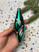 A hand is holding a green glass ornament with a floral design, surrounded by colorful confetti on a white background.