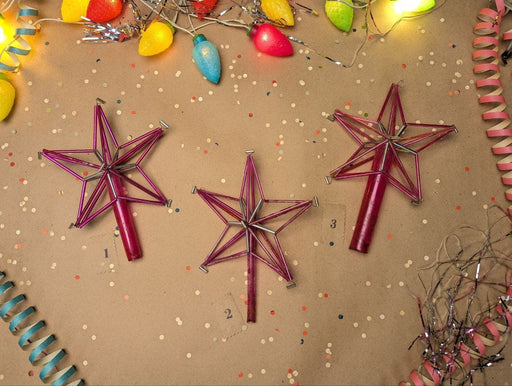 three pink star-shaped ornaments arranged on a brown background, surrounded by colorful confetti and twinkling lights.
