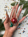 A hand holding a Christmas ornament with a red and green color scheme, surrounded by pine branches and confetti.