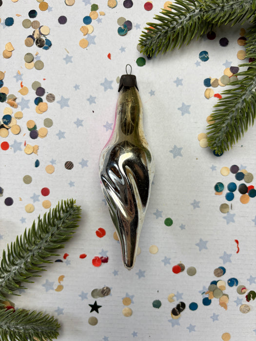 a silver ornament with a pointed end, surrounded by colorful confetti and green pine branches.