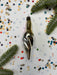 a silver ornament with a pointed end, surrounded by colorful confetti and green pine branches.