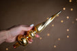 A hand holding a golden ornament with a pointed end, against a background of blurred lights.