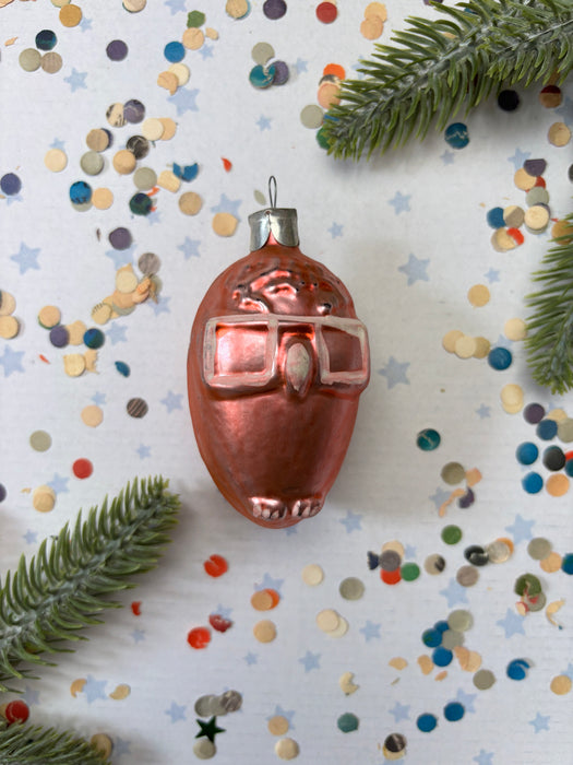 a shiny, metallic ornament resembling a small animal, surrounded by colorful confetti and green pine branches.