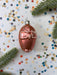 a shiny, metallic ornament resembling a small animal, surrounded by colorful confetti and green pine branches.