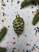 A shiny gold ornament with a bunch of small balls is displayed against a background of colorful confetti and pine branches.