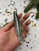 A hand holding a metallic object with a textured surface, surrounded by colorful confetti and a sprig of greenery.