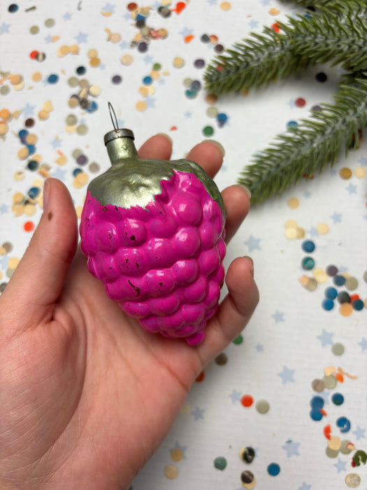 A hand holding a pink, berry-shaped ornament against a background of colorful confetti.