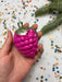 A hand holding a pink, berry-shaped ornament against a background of colorful confetti.