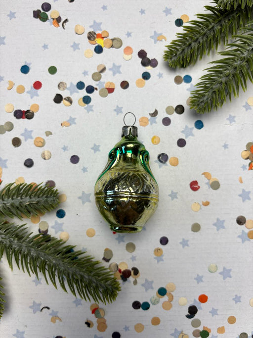 a green glass ornament with a reflective surface, surrounded by scattered multicolored confetti and green pine branches.
