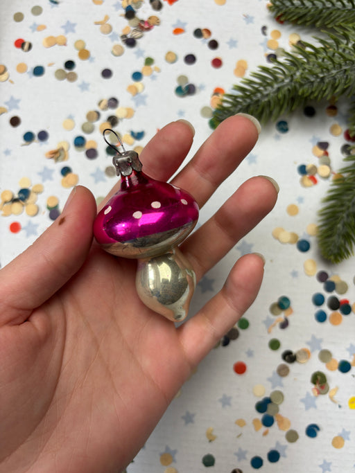 A hand holding a pink and silver ornament with polka dots against a background of colorful confetti.