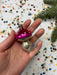 A hand holding a pink and silver ornament with polka dots against a background of colorful confetti.