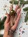 A hand holding a metallic object with a pointed end, surrounded by pine branches and confetti on a white background.