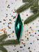 a green ornament, possibly a Christmas ornament, surrounded by colorful confetti and pine branches.