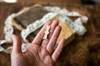 A hand holding a small white rabbit charm against a blurred background of books and lace.