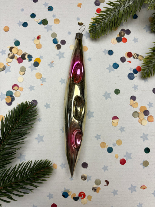 a shiny, metallic ornament resembling a canoe or kayak, surrounded by colorful confetti and pine branches.