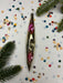 a shiny, metallic ornament resembling a canoe or kayak, surrounded by colorful confetti and pine branches.