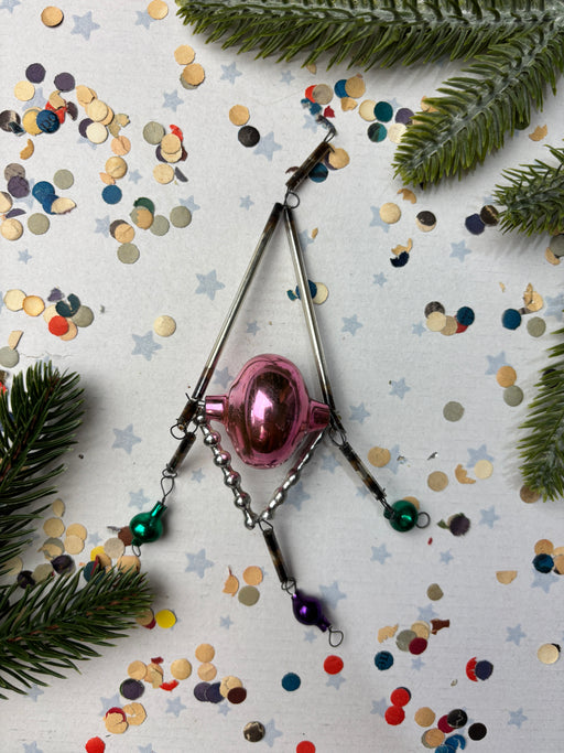 a pink ornament, a silver wire, and a collection of colorful confetti on a white background.