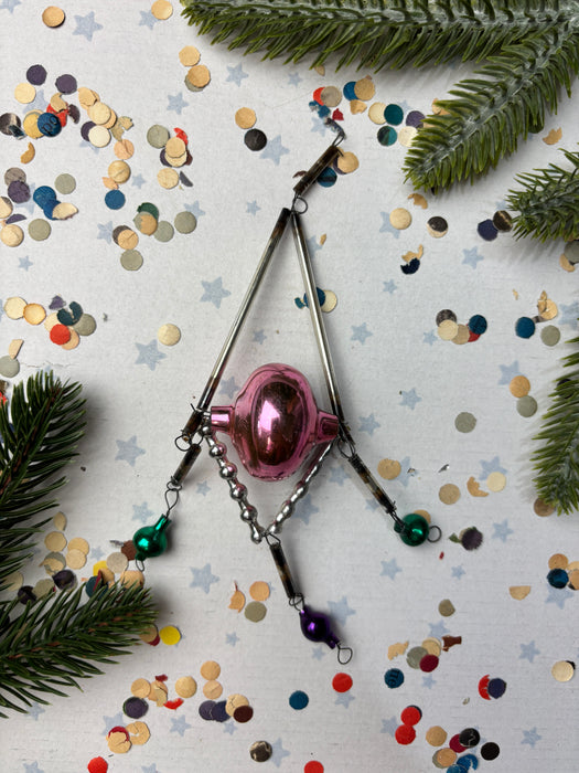 a pink ornament, a silver wire, and a collection of colorful confetti on a white background.