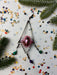 a pink ornament, a silver wire, and a collection of colorful confetti on a white background.