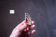 A hand holding a decorative piece of jewelry, possibly a ring or brooch, against a dark background.